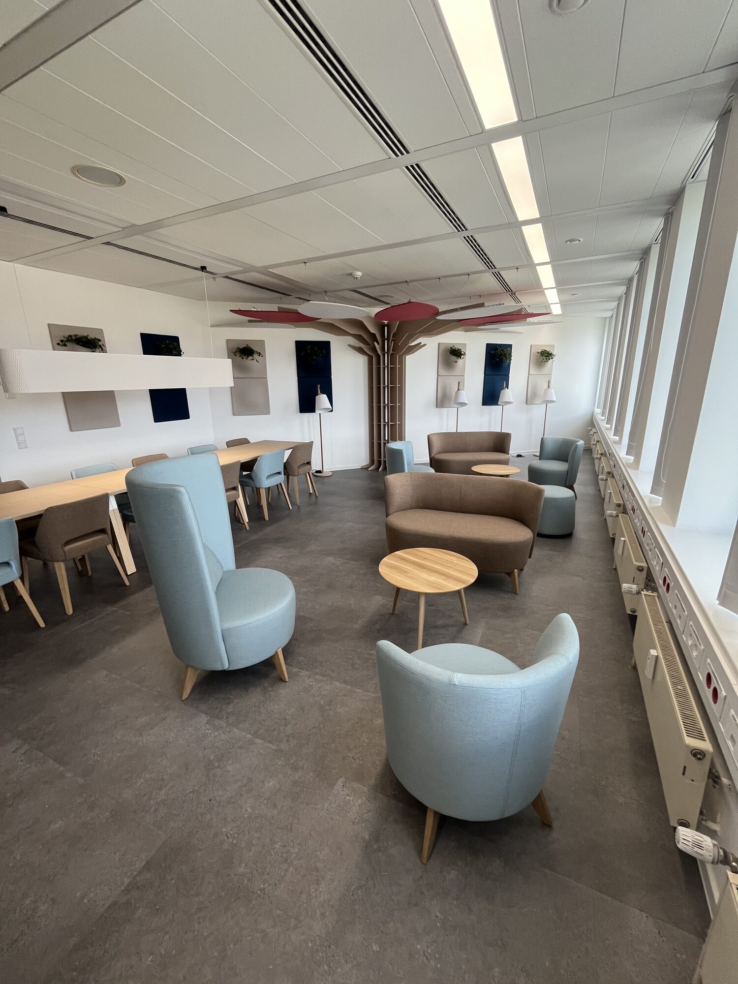 Lounge-Bereich mit hellblauen Sesseln, Sofas, runden Holztischen und Baum-Akustikelement